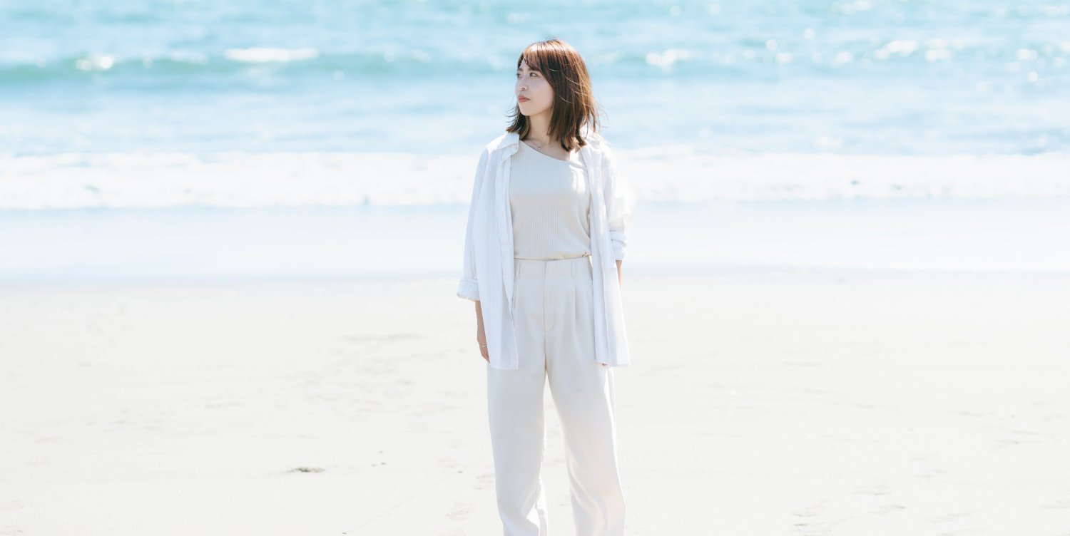 ビーチに立ち海を眺める白い服装のmomokaさん
