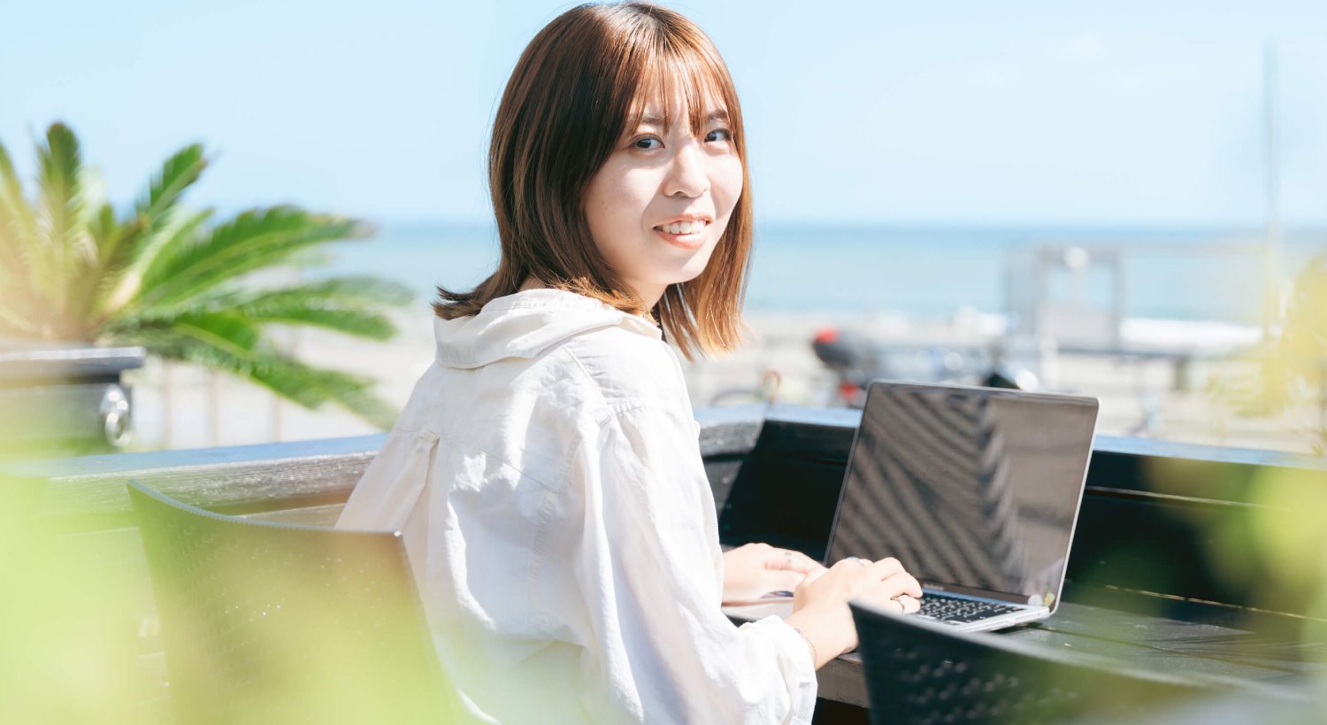 海辺のテラスでノートPCに向かい振り返って微笑むmomokaさん