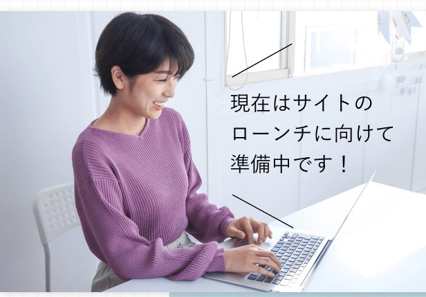 ノートPCのキーボードを操作するまゆみさんのデスクでの作業風景。写真内に「現在はサイトのローンチに向けて準備中です！」というテキストバーが焼き込まれている