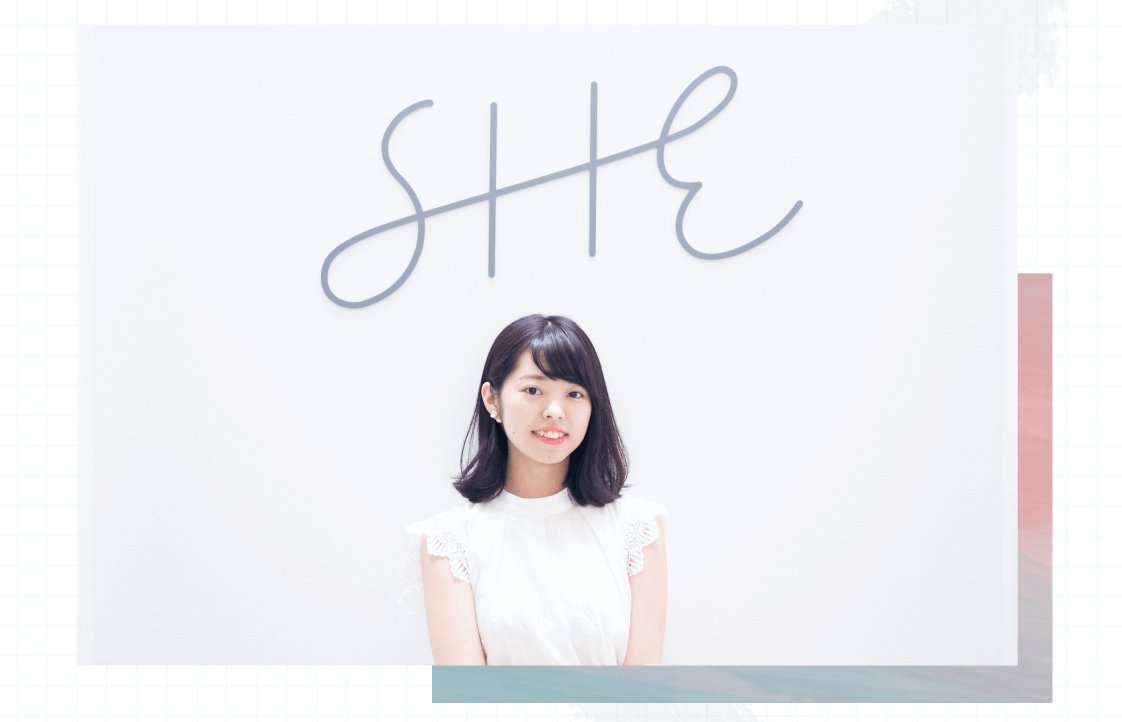 「SHE」の署名イラストの前で微笑む伊藤さんのポートレート