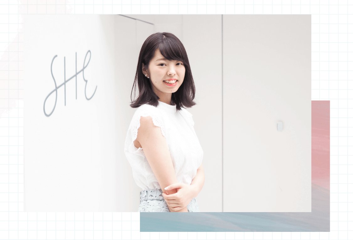 「SHE」の署名イラストの前で腕を組んで微笑む伊藤さんのポートレート