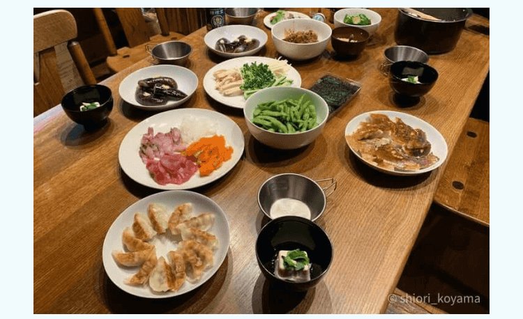 木のテーブルに並んだ和食の食事(刺身、餃子、味噌汁など)
