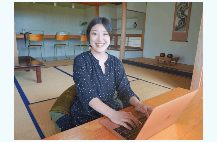 和室の縁側でノートPCに向かい微笑む小山志織さん(ドット柄トップス)
