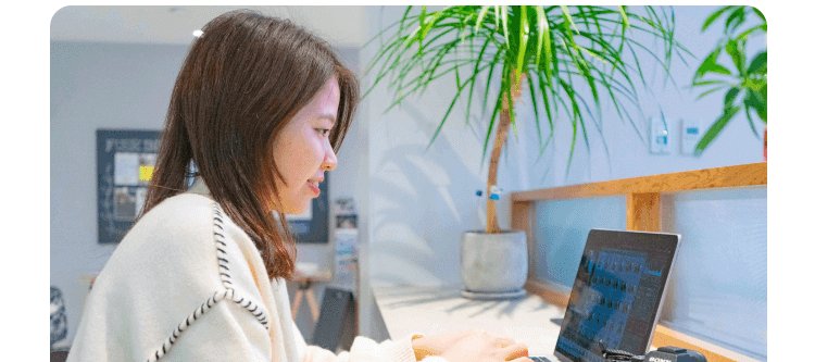 観葉植物と木製カウンターのある空間で、ノートPCに向かうかんなさんの横顔