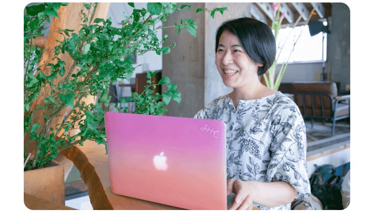 観葉植物のある店内でノートパソコンに向かい微笑むけいこさん