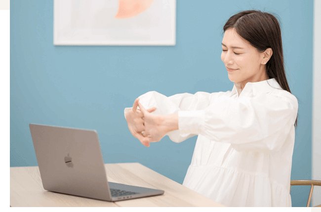 青い壁のオフィスで石井さんが両手を伸ばしてストレッチする写真