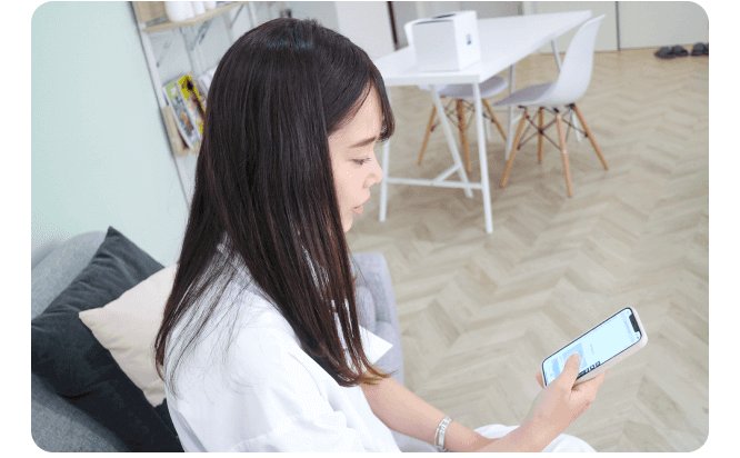 ソファに座りスマホを見る捺水さん(部屋の一室)