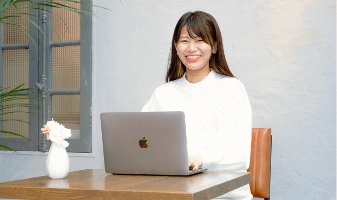 窓辺のデスクでノートPCに向かい微笑む愛実さん