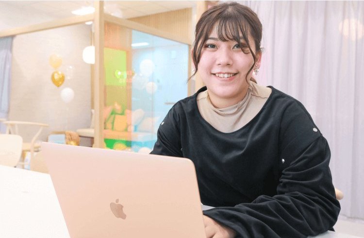 バルーン装飾のある教室でノートパソコンに向かって微笑む竹田凜さん