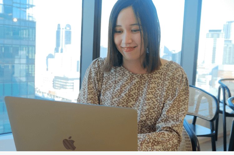高層ビルの窓際でノートPCに向かい微笑むみづきさん
