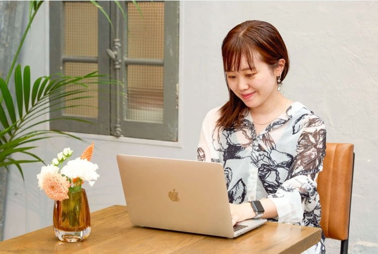 木製テーブルでノートPCに向かい微笑む愛弓さん