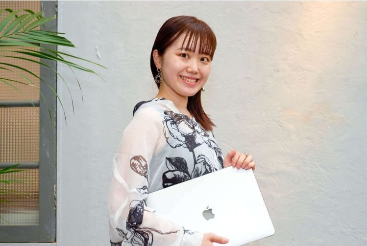 屋外でノートPCを抱えて振り返り微笑む愛弓さん