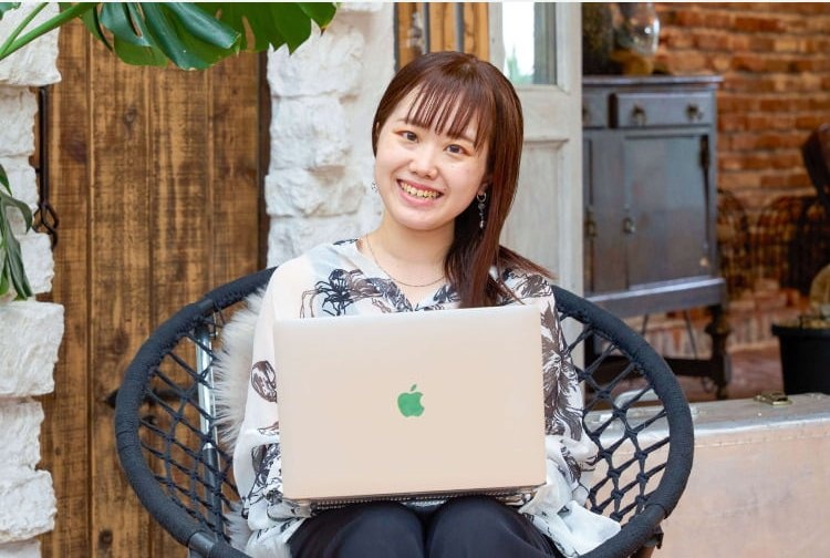 ラタンチェアに座りノートPCを抱えて微笑む愛弓さん