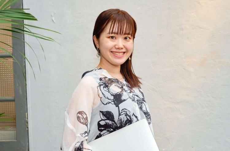 屋外でノートPCを抱えて微笑む愛弓さん
