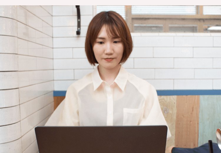 白いタイル壁を背にノートパソコンに向かうかのりさん