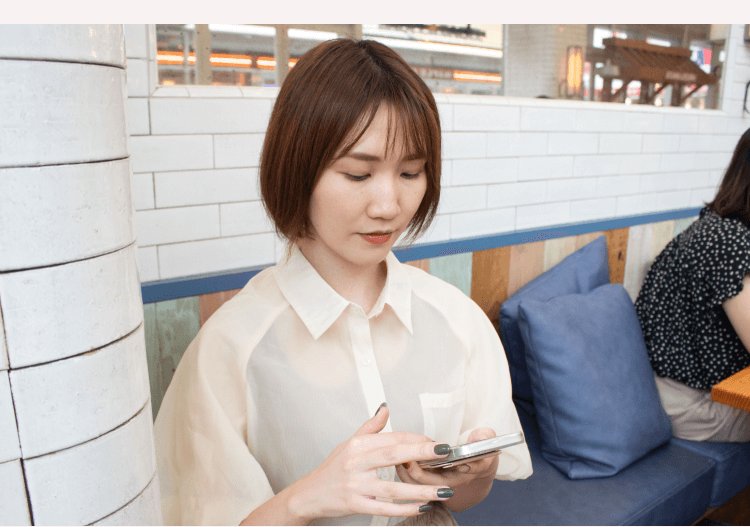 カフェの座席でスマートフォンを操作するかのりさん