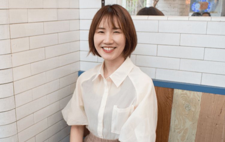 白いタイル壁を背に微笑むかのりさん