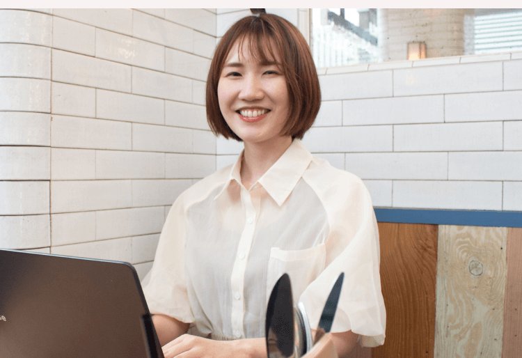 白いタイル壁を背にノートパソコンに向かい微笑むかのりさん