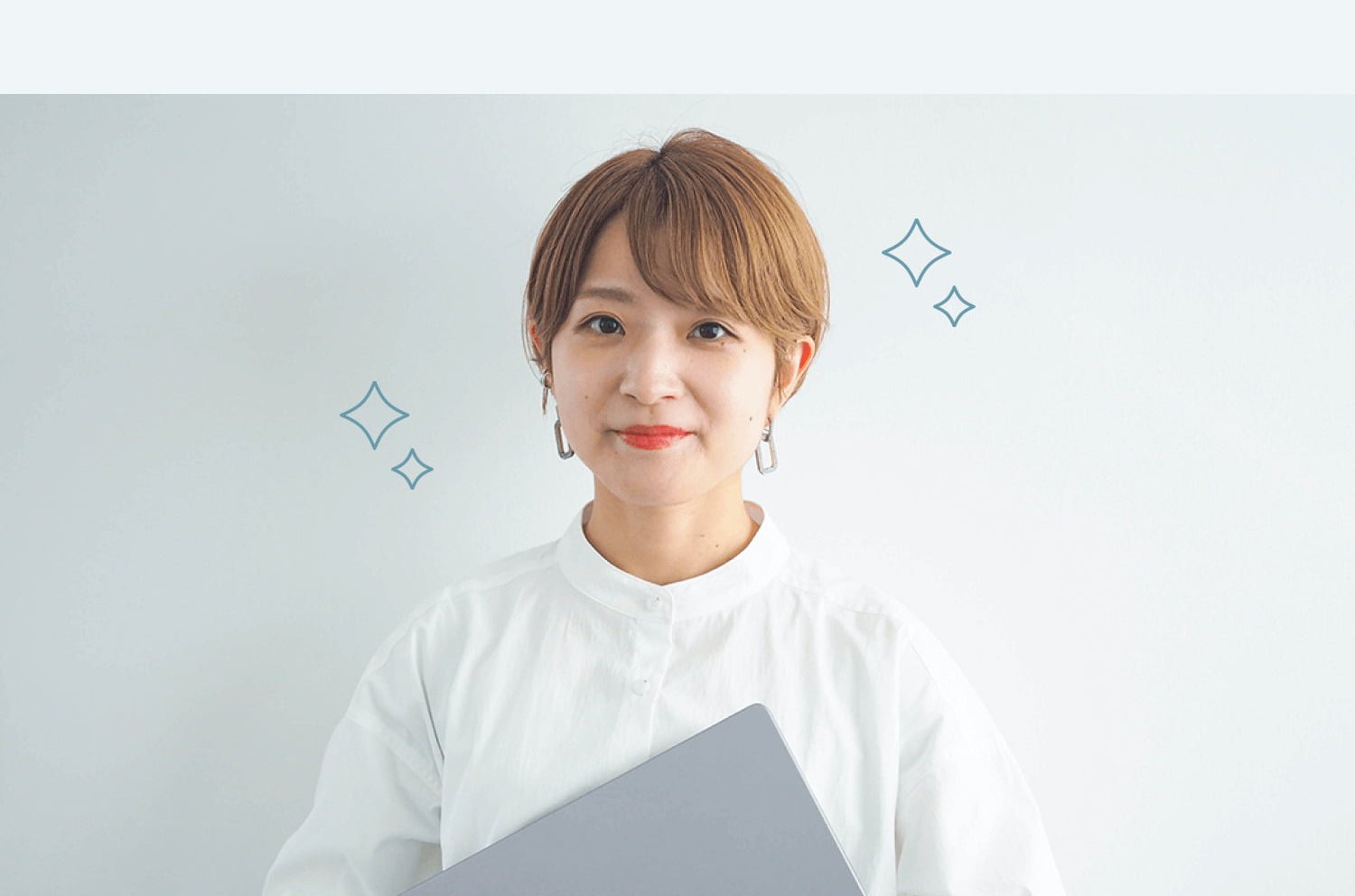 ノートPCを抱えて微笑む白シャツの女性