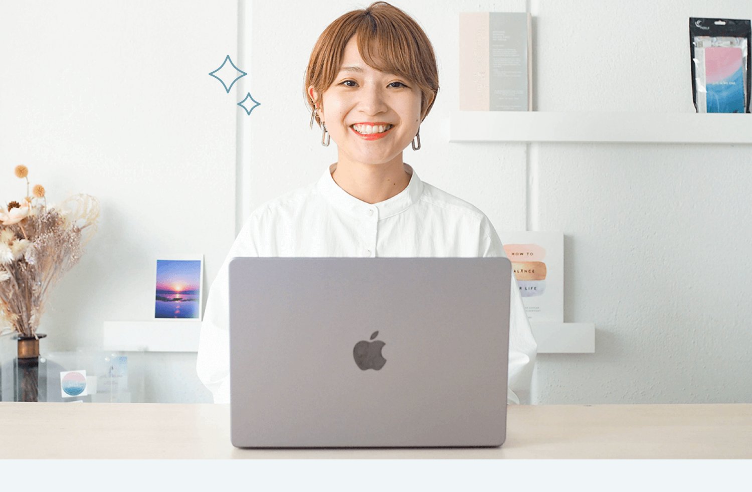 ノートPCの前で微笑む白シャツの女性