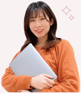 ノートPCを抱えて微笑むオレンジニットの女性（After、キラキラ装飾付き）