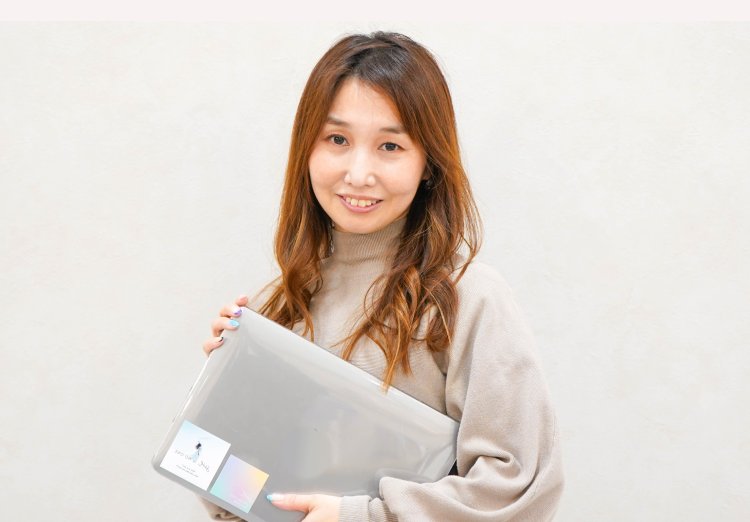 ノートPCケースを抱えて微笑むのんさんのポートレート