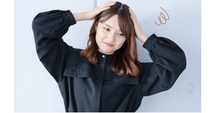 白い壁を背に両手で頭を抱える女性(不安な表情)