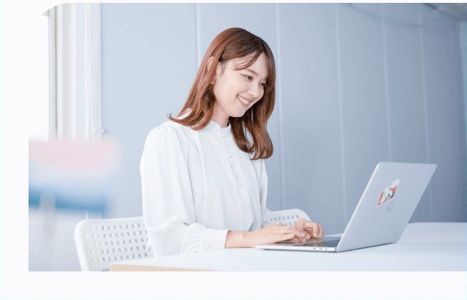 白いテーブルでノートPCに向かい入力しながら微笑む女性