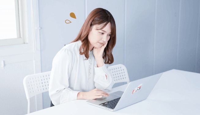 白いテーブルでノートPCの前に座り、頬杖をついて考え込む女性
