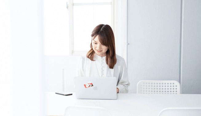 白いテーブルでノートPCに向かう女性、明るい室内