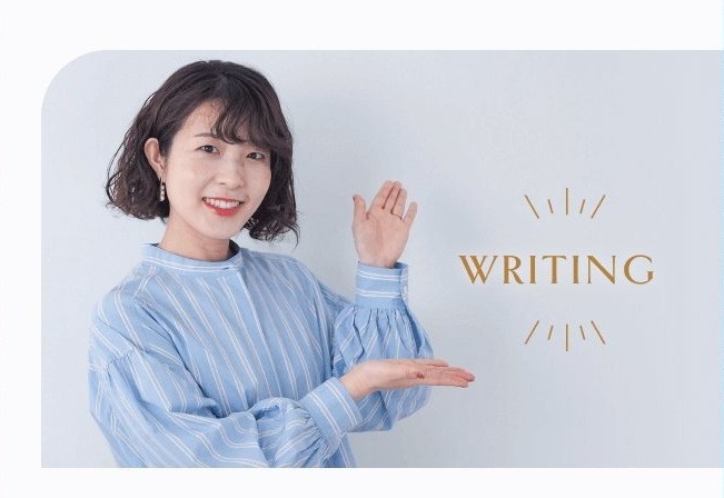 WRITINGの文字とともに手のひらを見せる萌さん