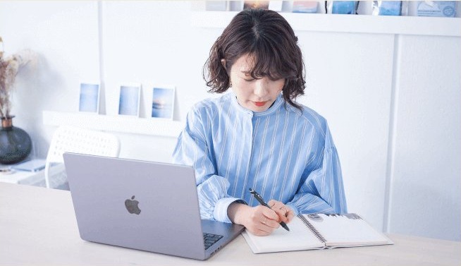 手帳に書き込みながらノートパソコンに向かう萌さん