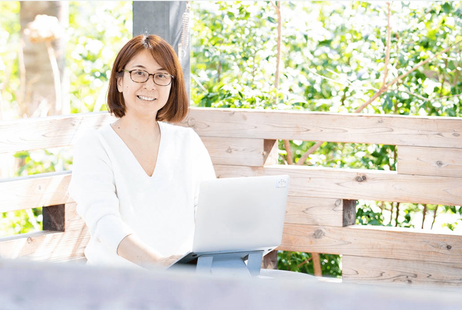 木製ベンチに座りノートパソコンを操作しながら微笑む美緒さん