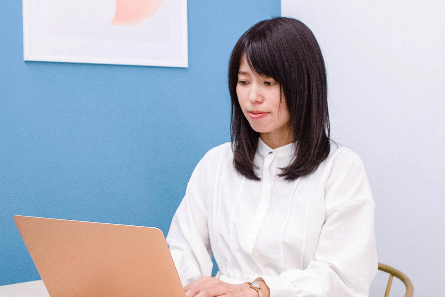 青い壁の前でノートパソコンを操作する女性