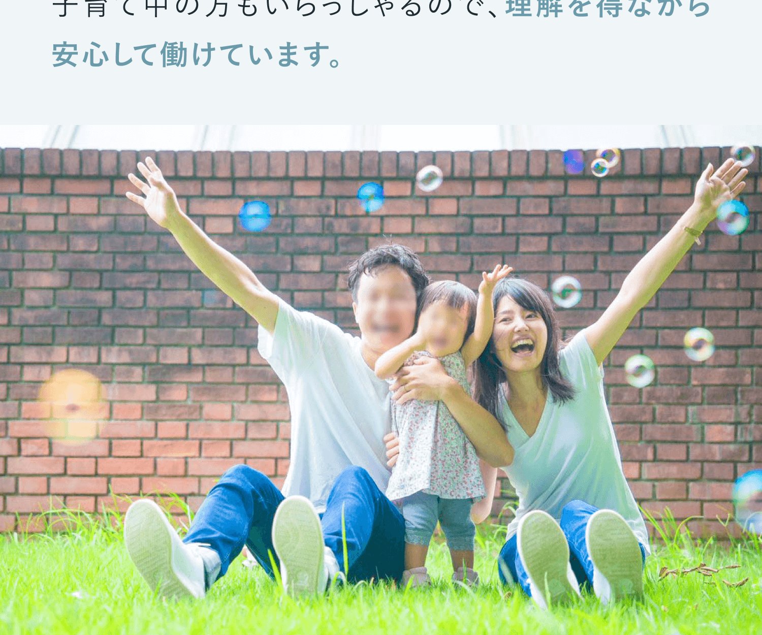 レンガ塀の前、芝生に座って両手を挙げ喜ぶ家族