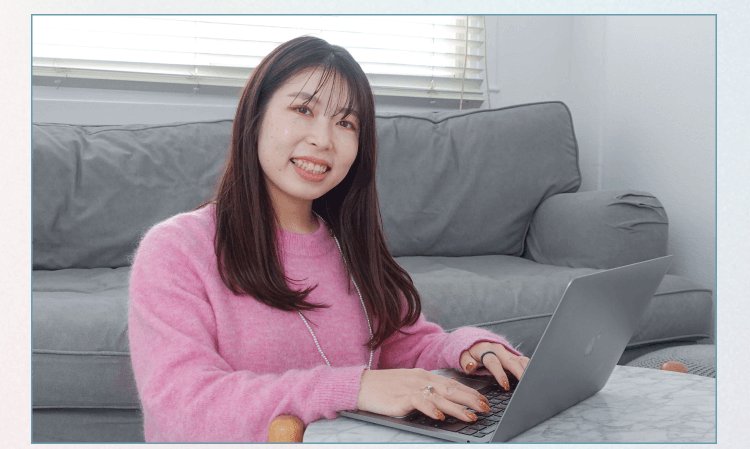 ソファ前でノートパソコンを操作しながら微笑むyurieさん（ピンクのニット）