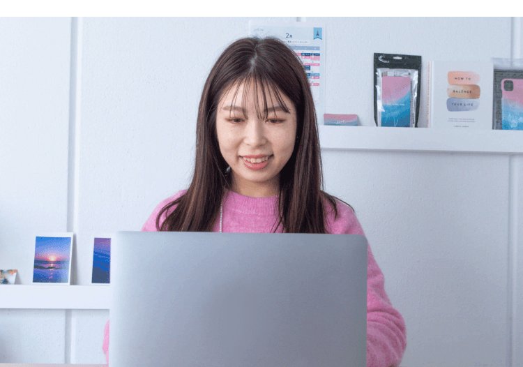 自宅の棚の前でノートパソコンに向かうyurieさん（雑貨・小物が並ぶ棚が背景）
