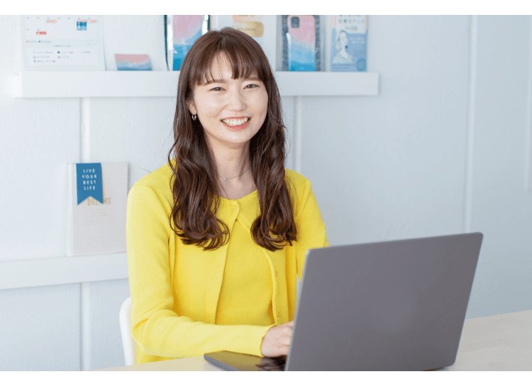 パソコン棚の前でノートPCを操作する黄色カーディガンの女性