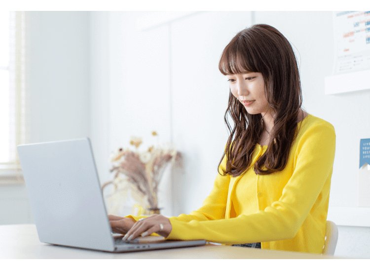 ソファでノートPCを操作する黄色カーディガンの女性の横顔