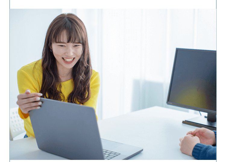 笑顔でノートPCを操作する黄色カーディガンの女性、対面に話しかける相手の手元