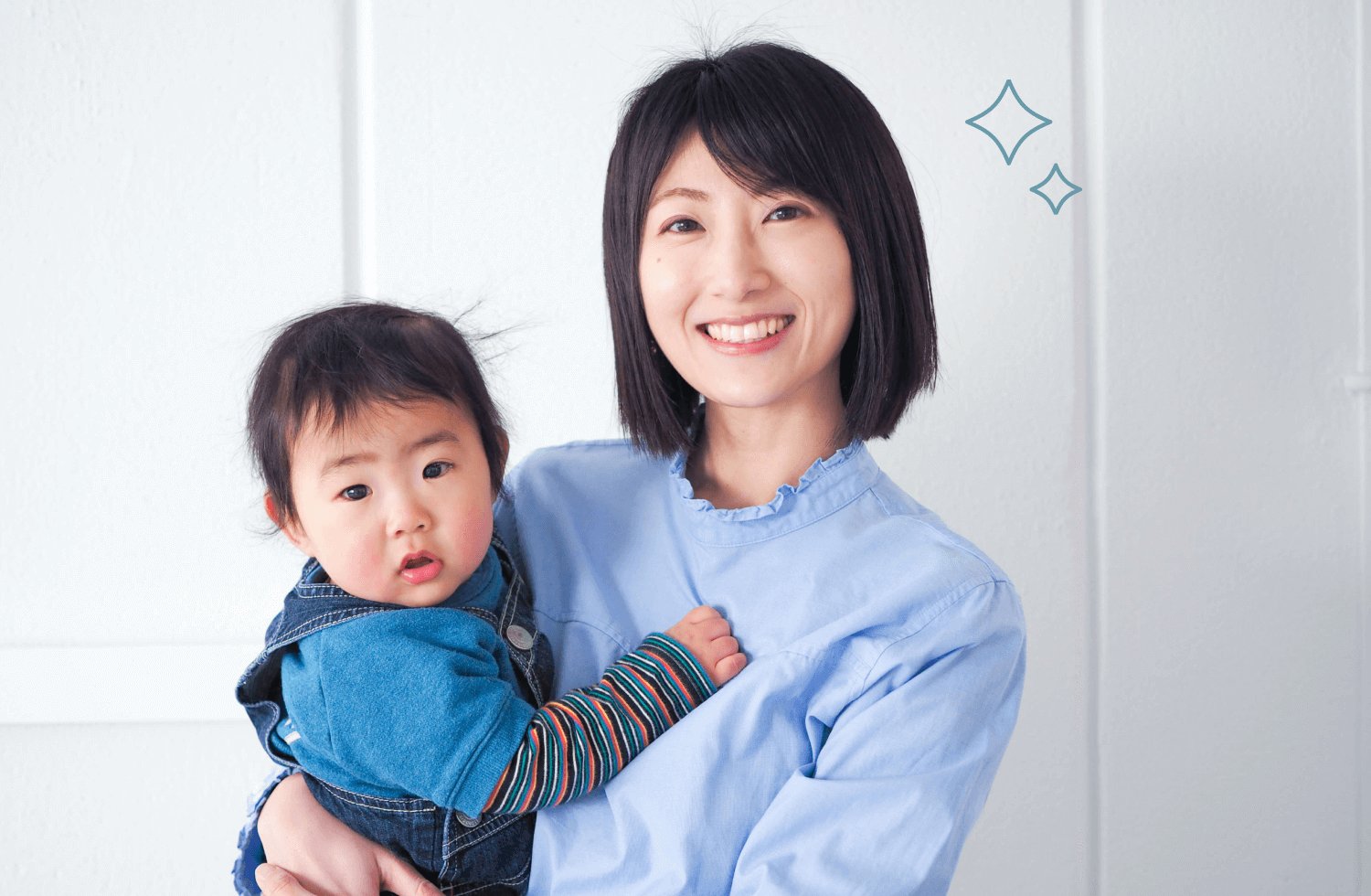 白い部屋で水色シャツのきゃんまりさんが微笑みながら子どもを抱く様子