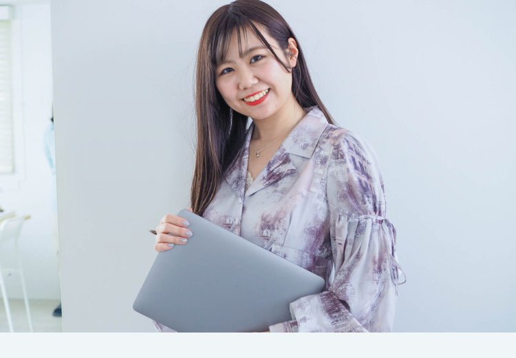 壁を背に、ノートパソコンを抱えて微笑むぴちゃんさん
