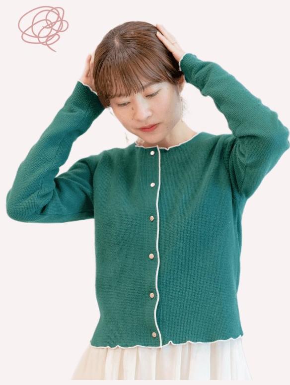 頭に両手を当て目を伏せる緑ニットの女性（Before）