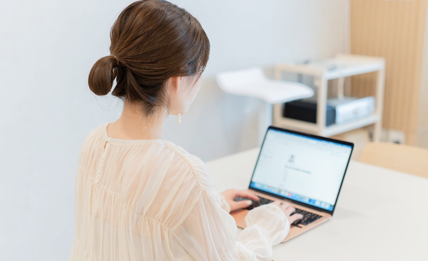 窓際でノートPCに向かって作業する女性の後ろ姿