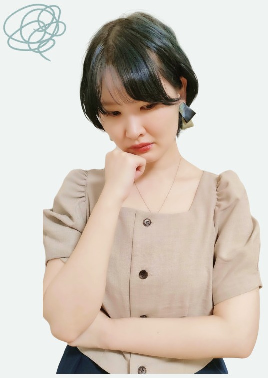 悩む表情で頬に手を当て腕を組む、もやもやマーク付きのベージュブラウスの人物（Before）