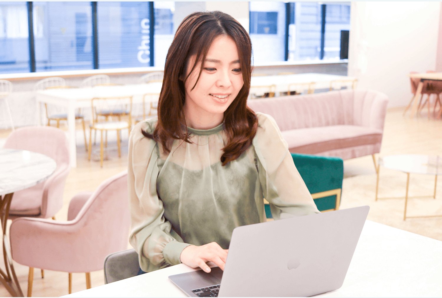 オフィスのソファ席でノートPCを操作しながら微笑む女性