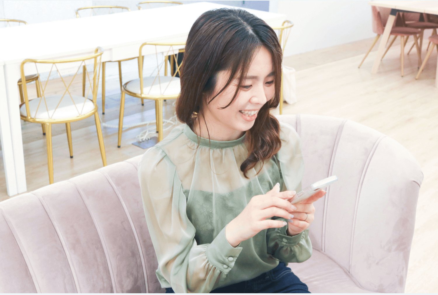 ピンクのソファに座りスマホを見て微笑む女性