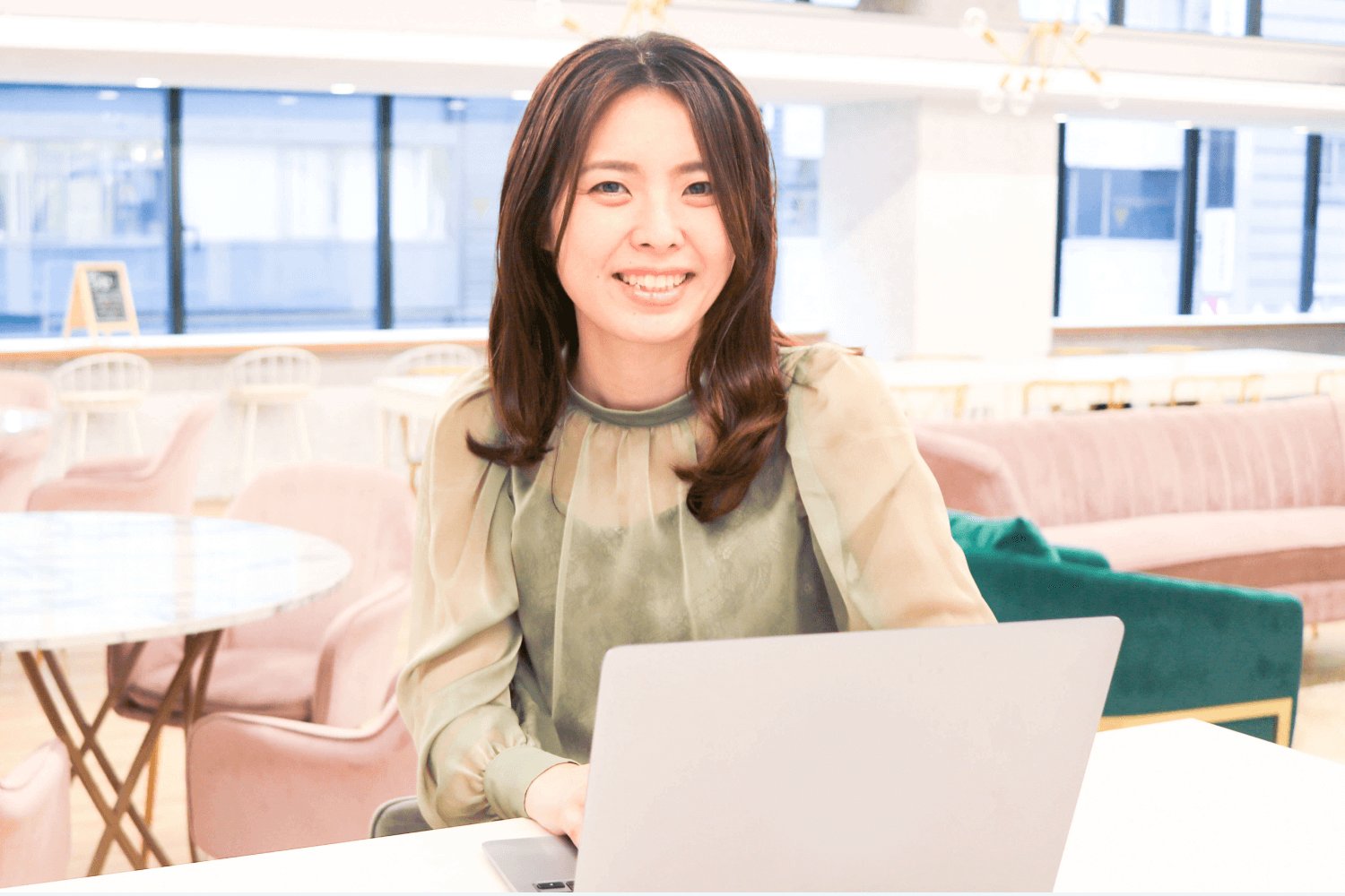 カフェのテーブルでノートPCに向かい正面を見て微笑む女性