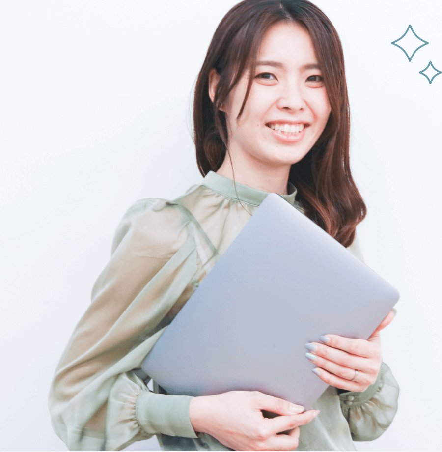 白い壁の前でノートPCを抱えて微笑む女性