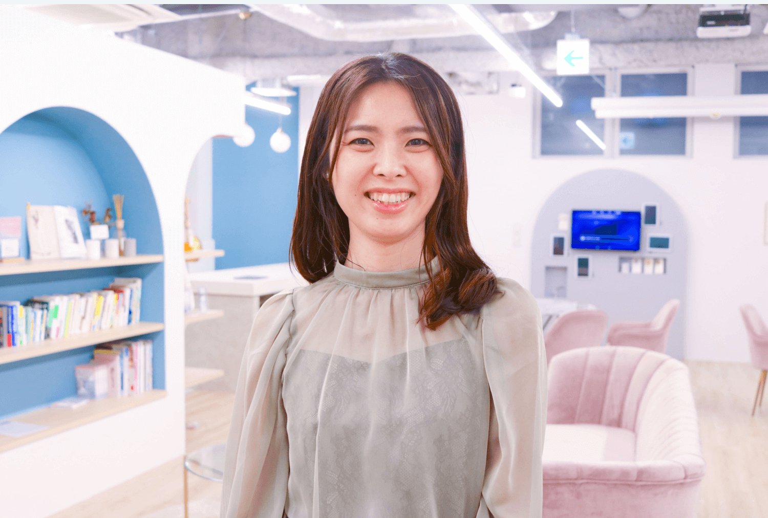 オフィスのアーチ型の棚の前に立ち微笑む女性のポートレート